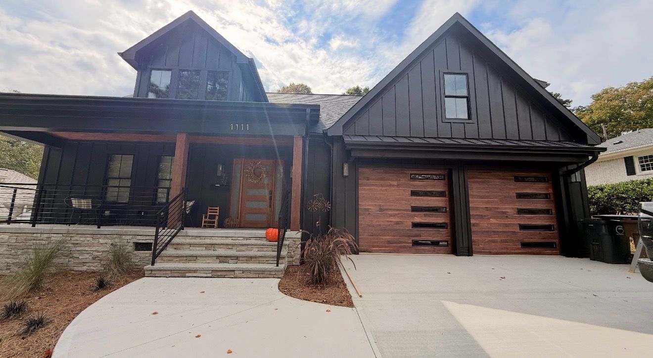 Two-story modern home with dark wood exterior, a front porch, and an attached two-car garage with wood accent doors.