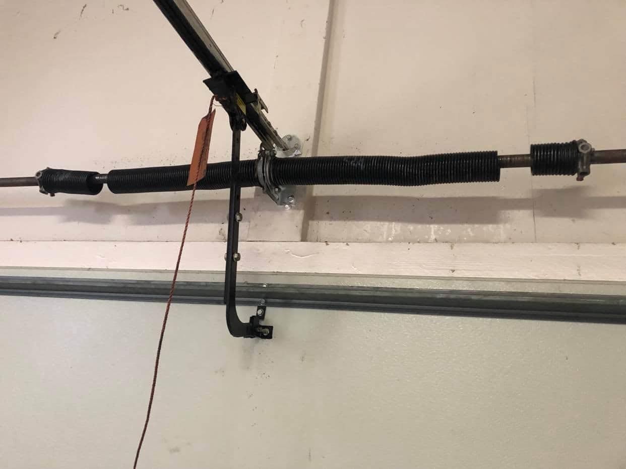 Garage door torsion spring assembly, black spring, metal rods, and cables.