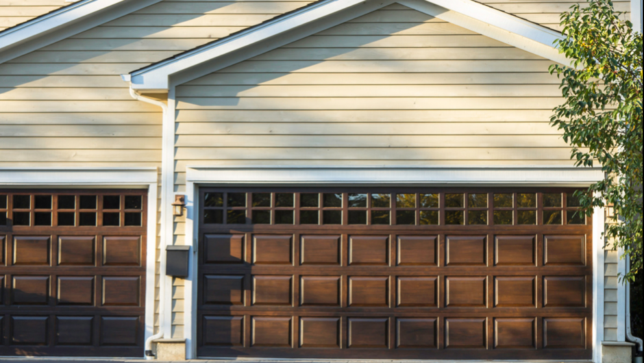 Two brown garage doors on a light yellow house with white trim.