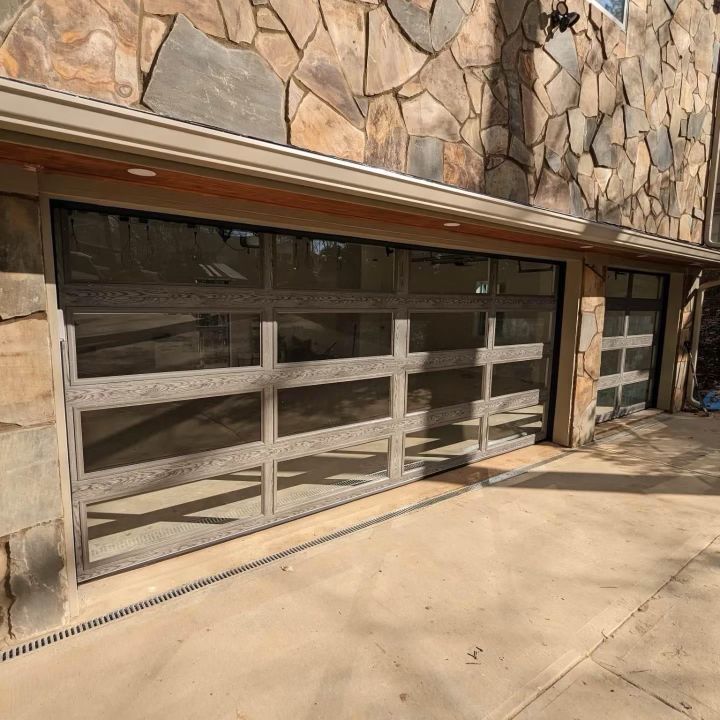 Two modern garage doors with tinted windows, set in a stone facade, on a concrete driveway.