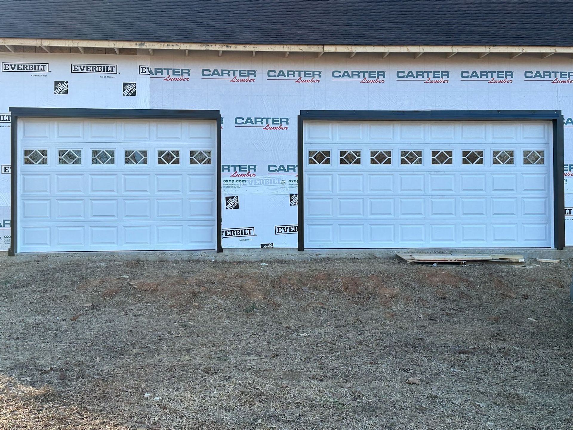 Two white garage doors with decorative windows, framed in black, on a new building under construction.