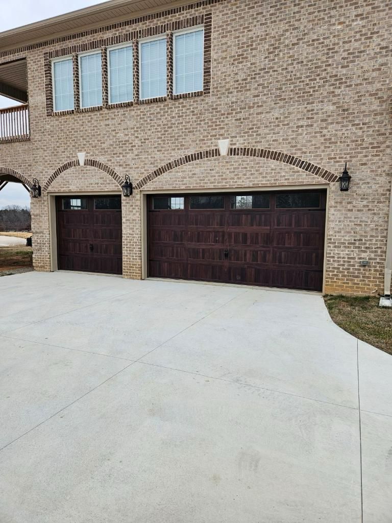 Two dark brown garage doors under brick arches on a light brick house with a concrete driveway.