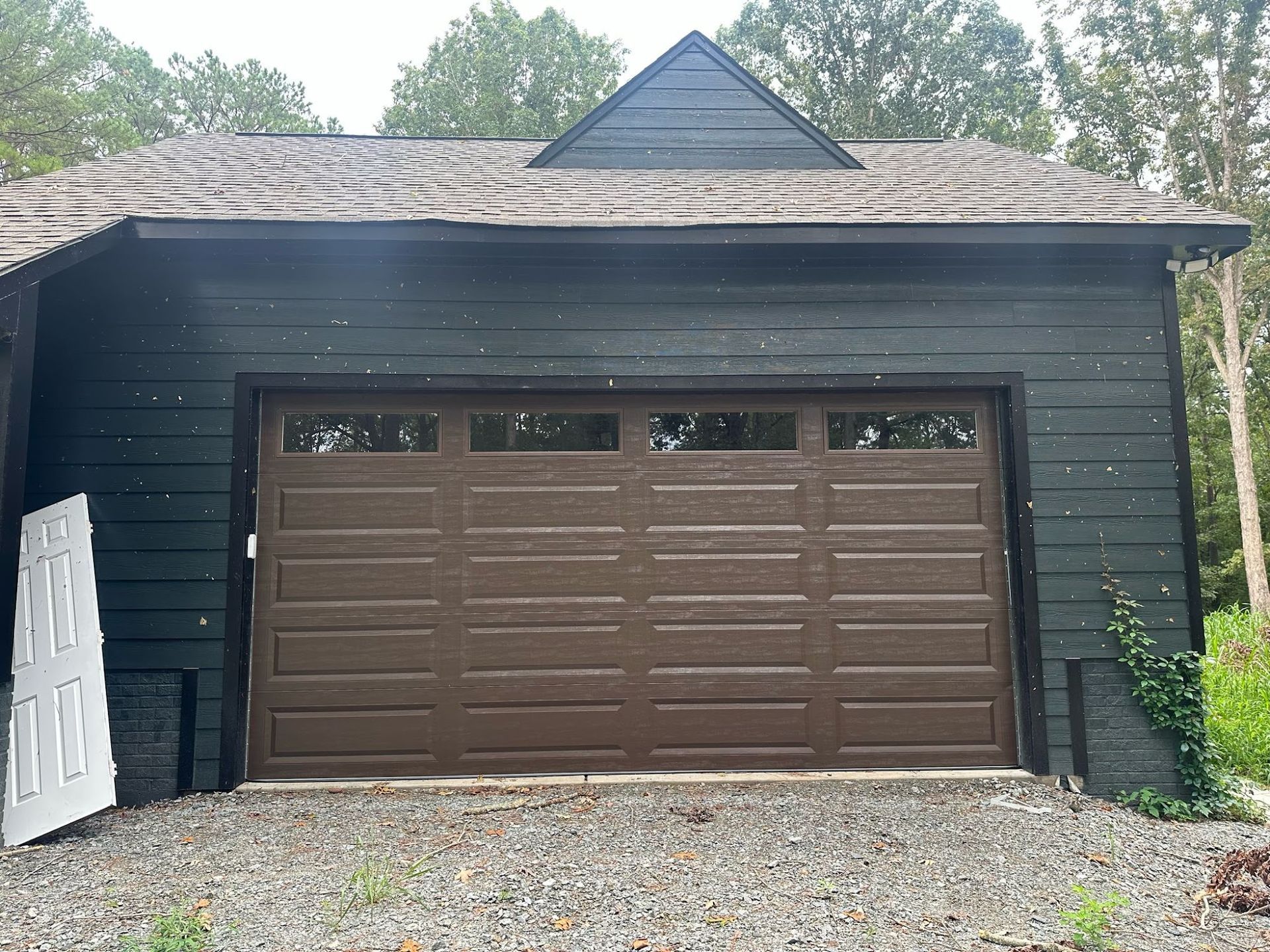 Brown garage door on a dark green building, gravel driveway.