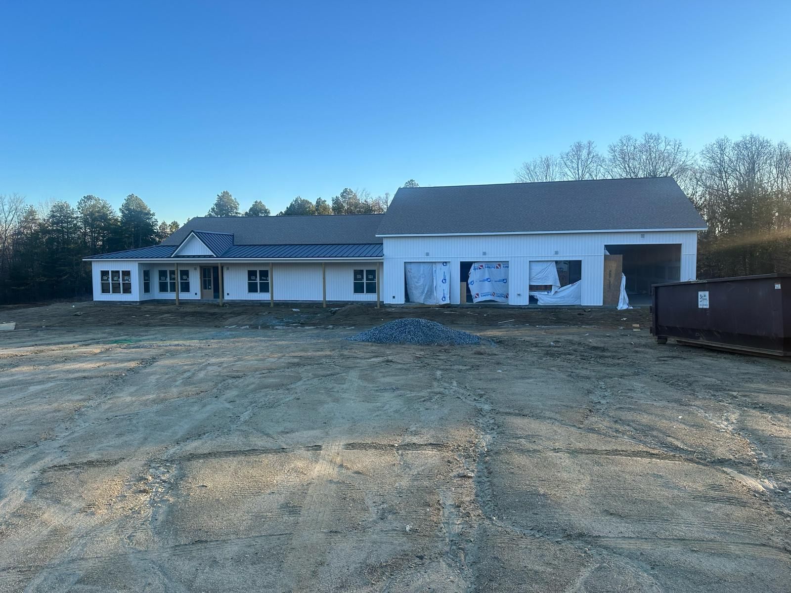 A newly constructed house with a detached garage on a dirt lot under a clear blue sky.