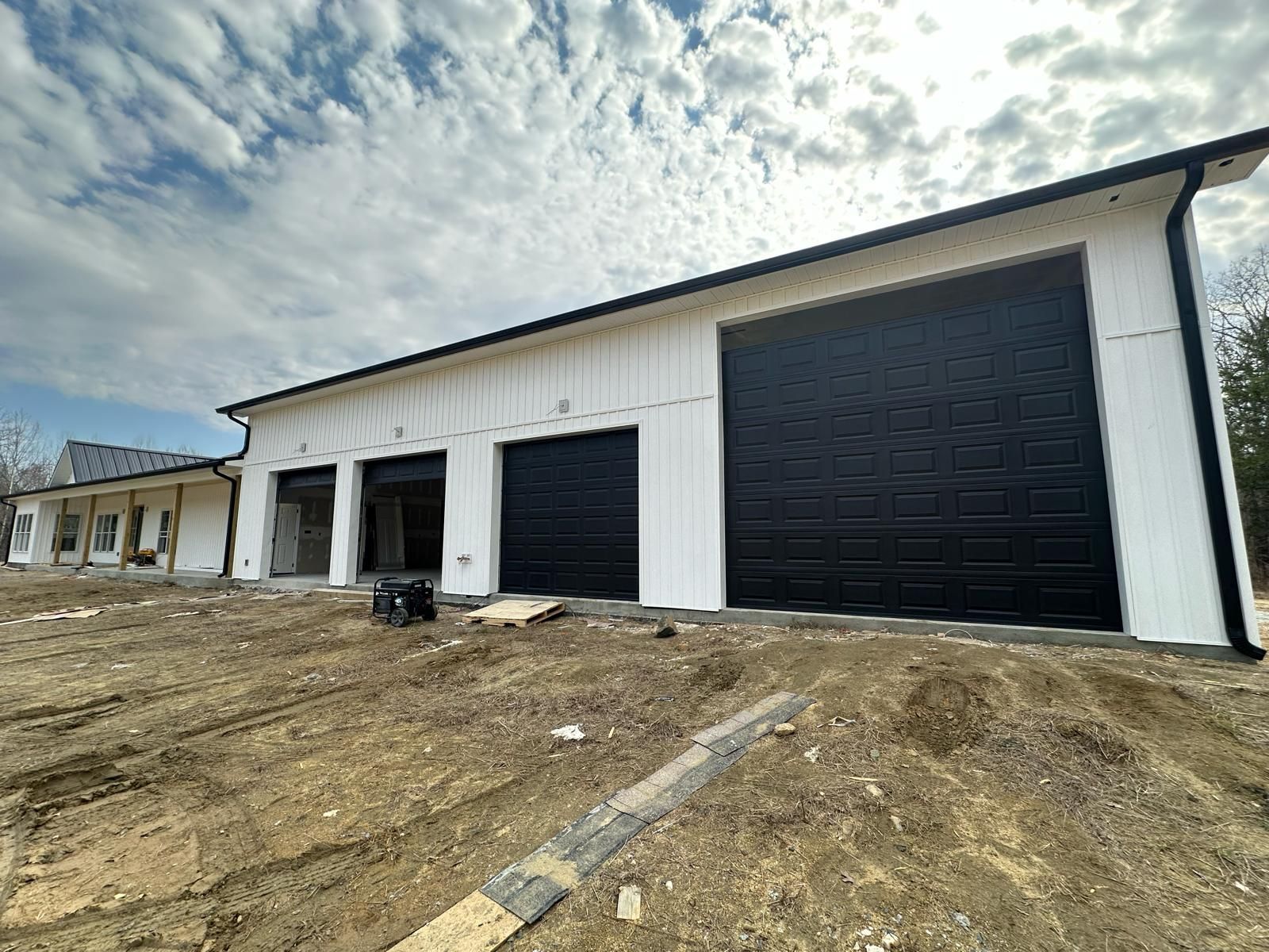 White building with three black garage doors under construction, cloudy sky.