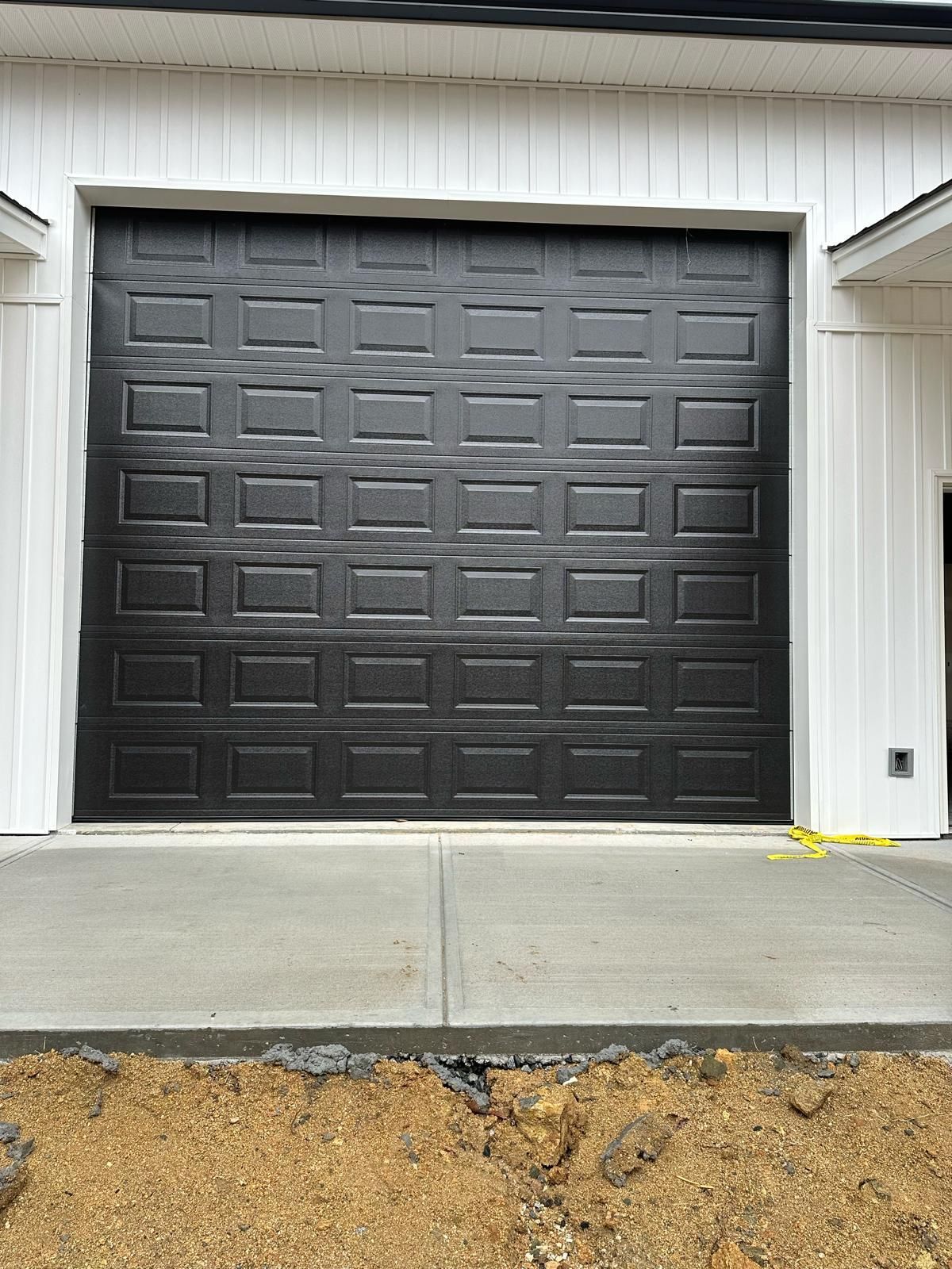Black garage door with square panels in a white-framed garage on a concrete slab; construction setting.