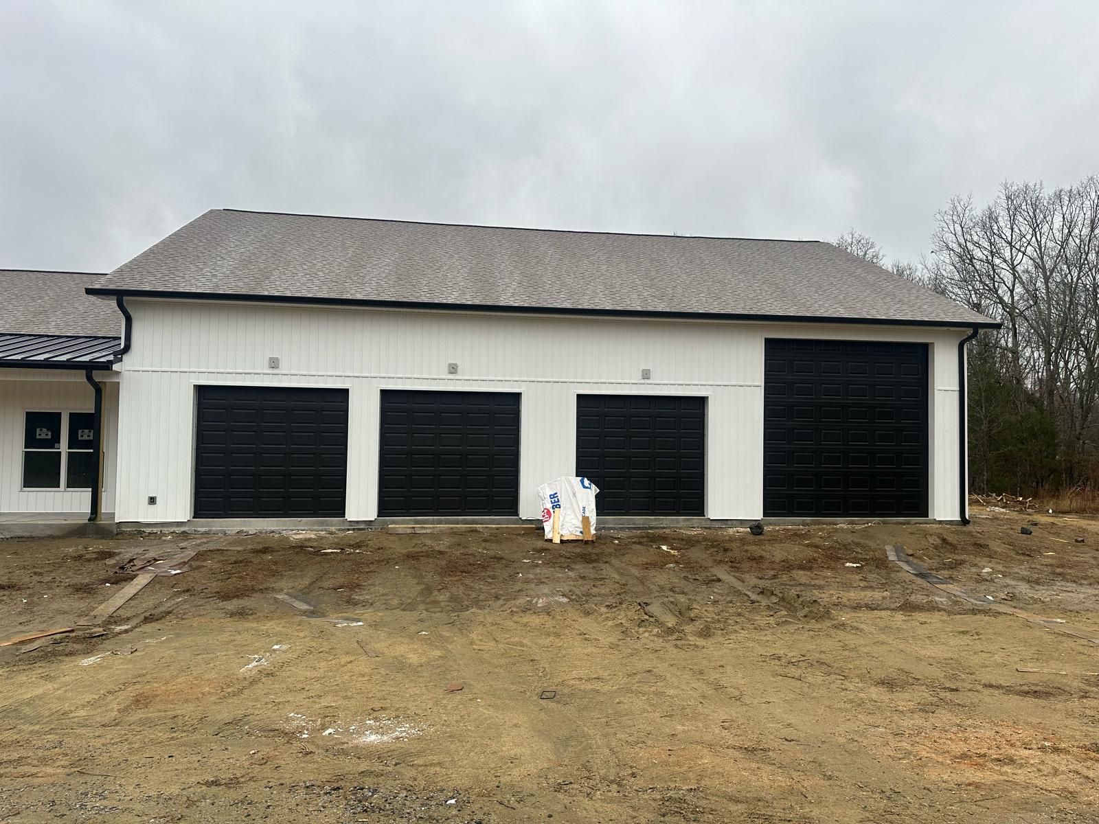 White building with three black garage doors and light brown roof.