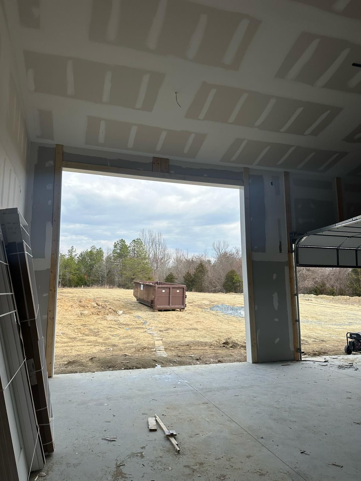 Open doorway in a building under construction, overlooking a field with a dumpster.