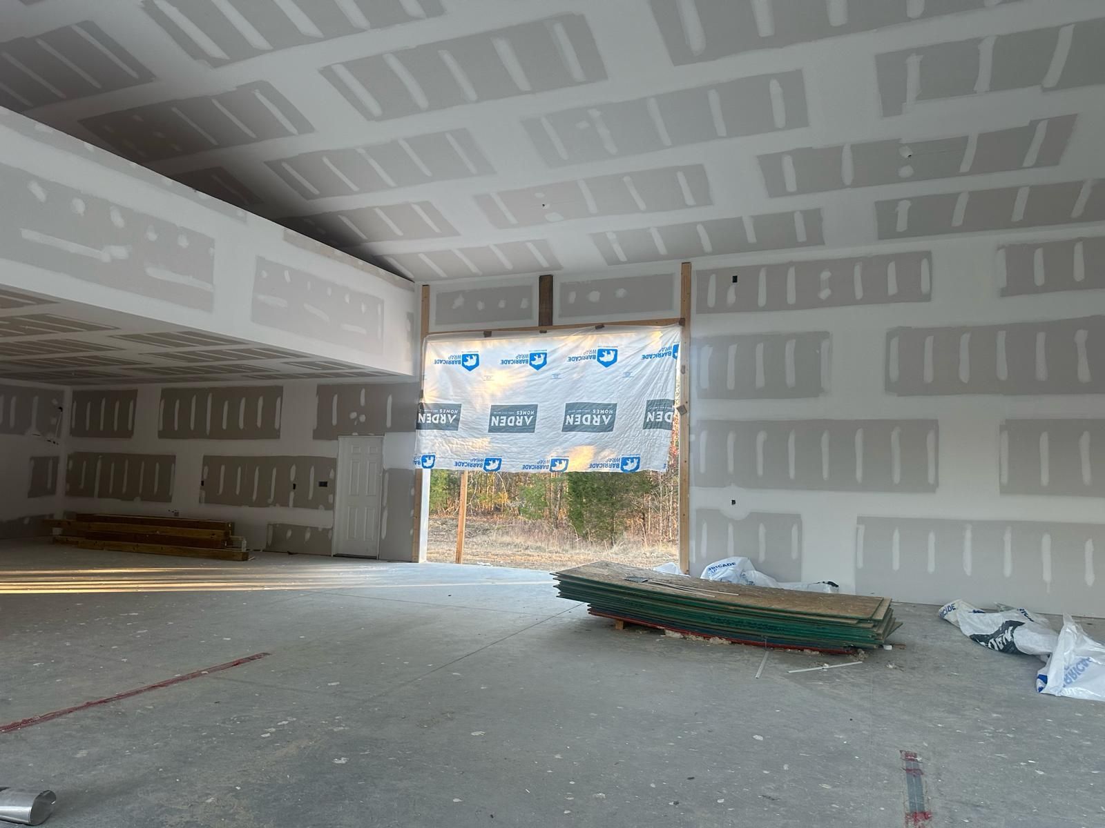 Interior of a building under construction, drywall installed on walls and ceiling, open doorway.