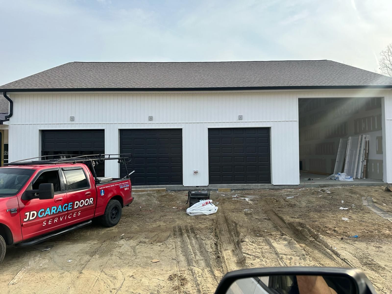 Three-car garage with black doors and white siding. A red truck is parked in front.