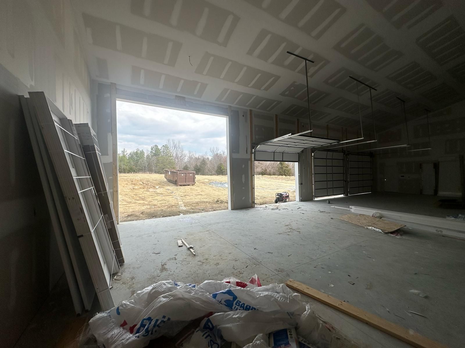 Interior of a building under construction, open doorway looking outside at a field, drywall and debris on the floor.