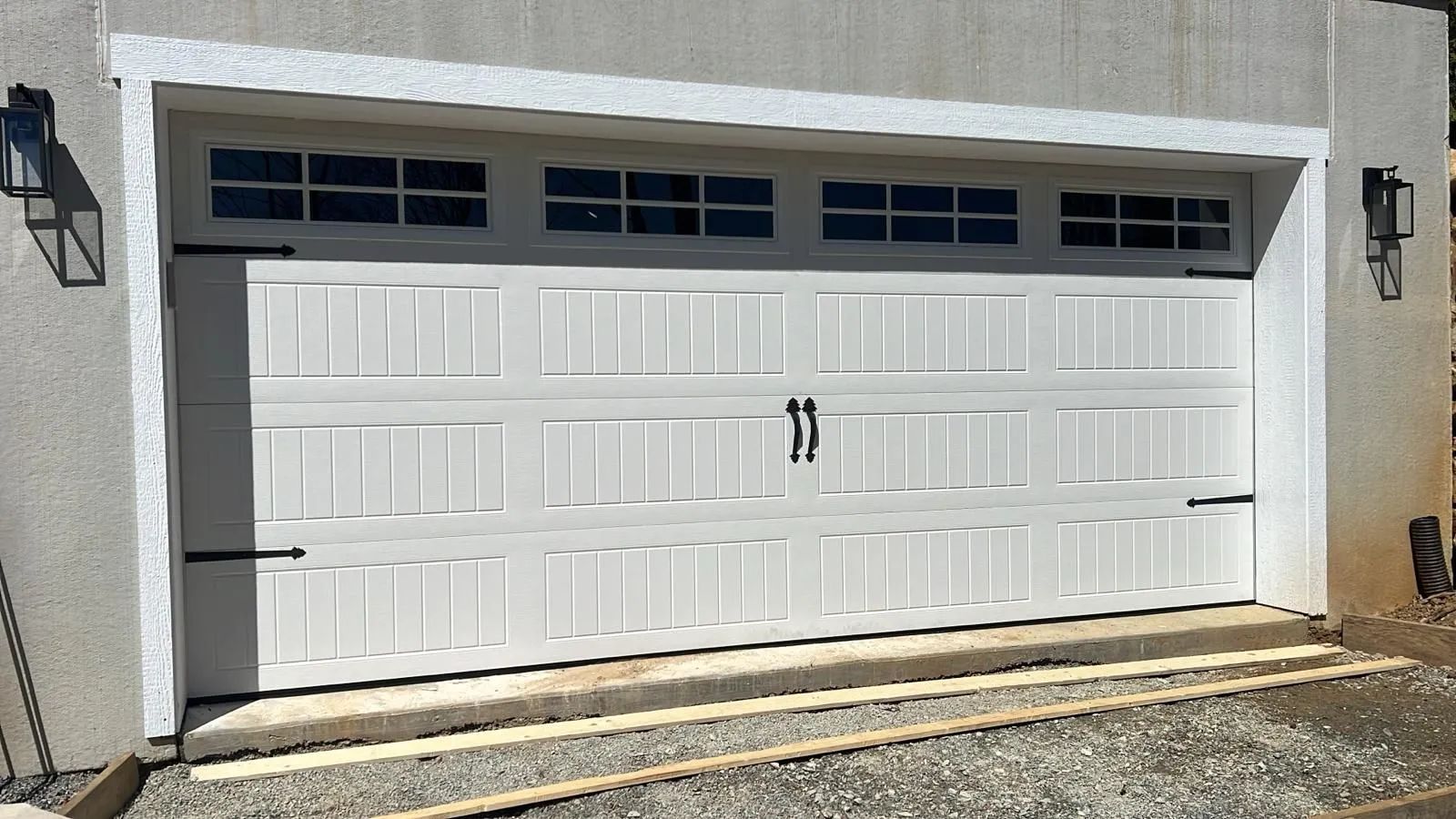 White garage door with rectangular windows, black hardware, and sconces.