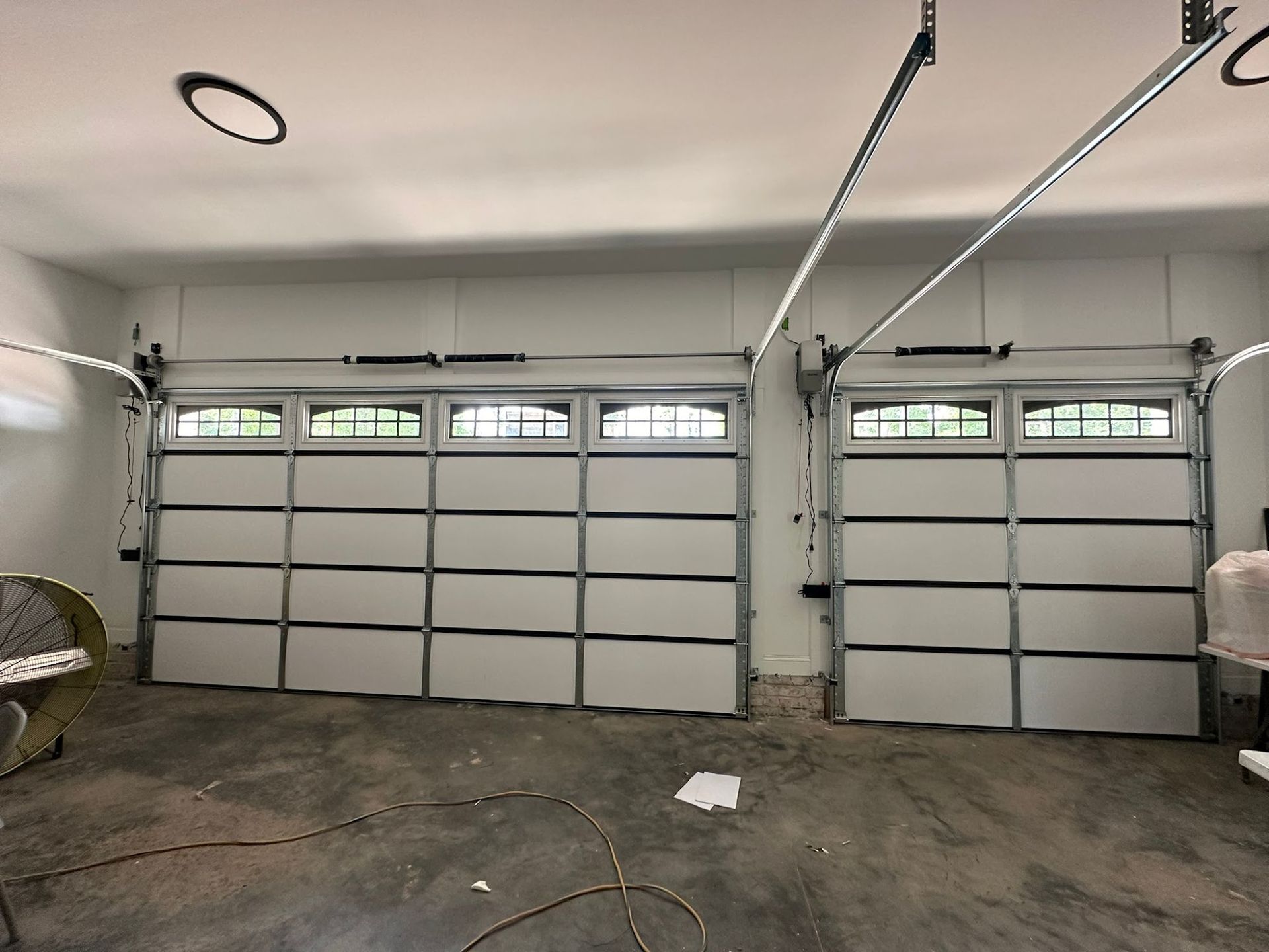 Two closed garage doors with windows, gray metal frames, and white panels in a garage.