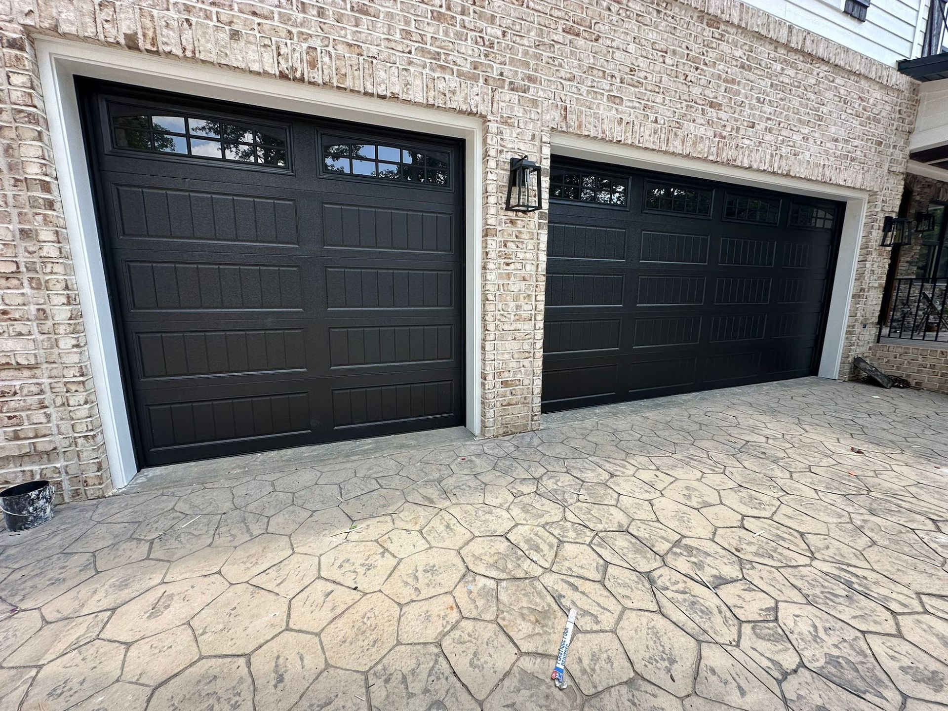 Two black garage doors with windows in a brick building with patterned concrete.