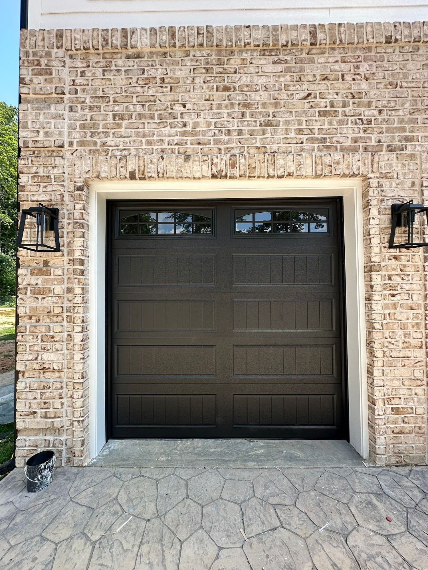Garage with brown door, framed by brick and white trim, with two black lanterns.