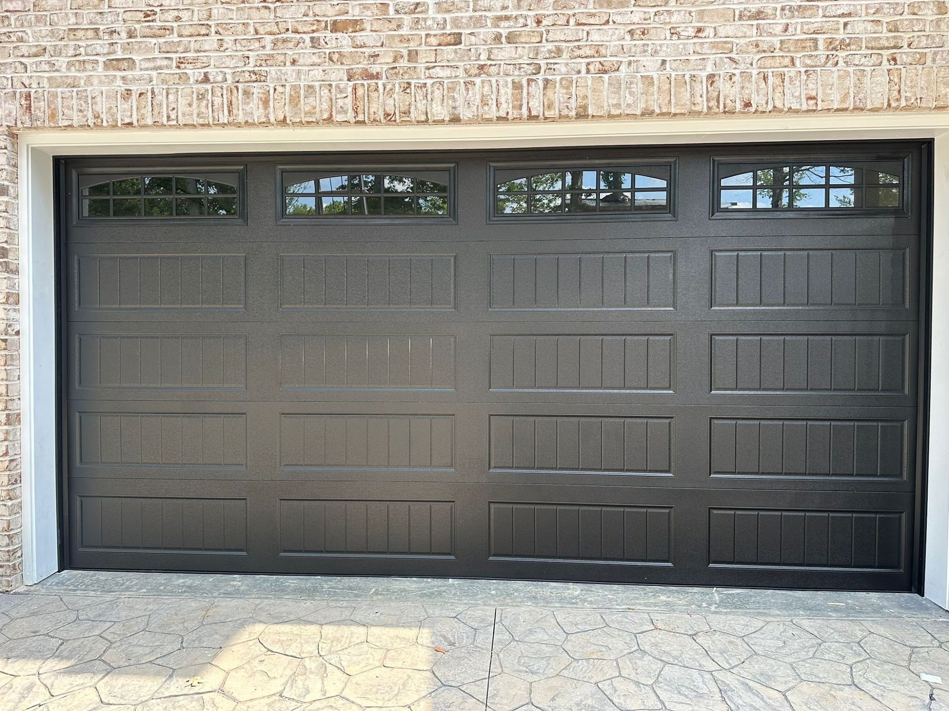 Dark gray garage door with windows, set in a brick and stone facade.