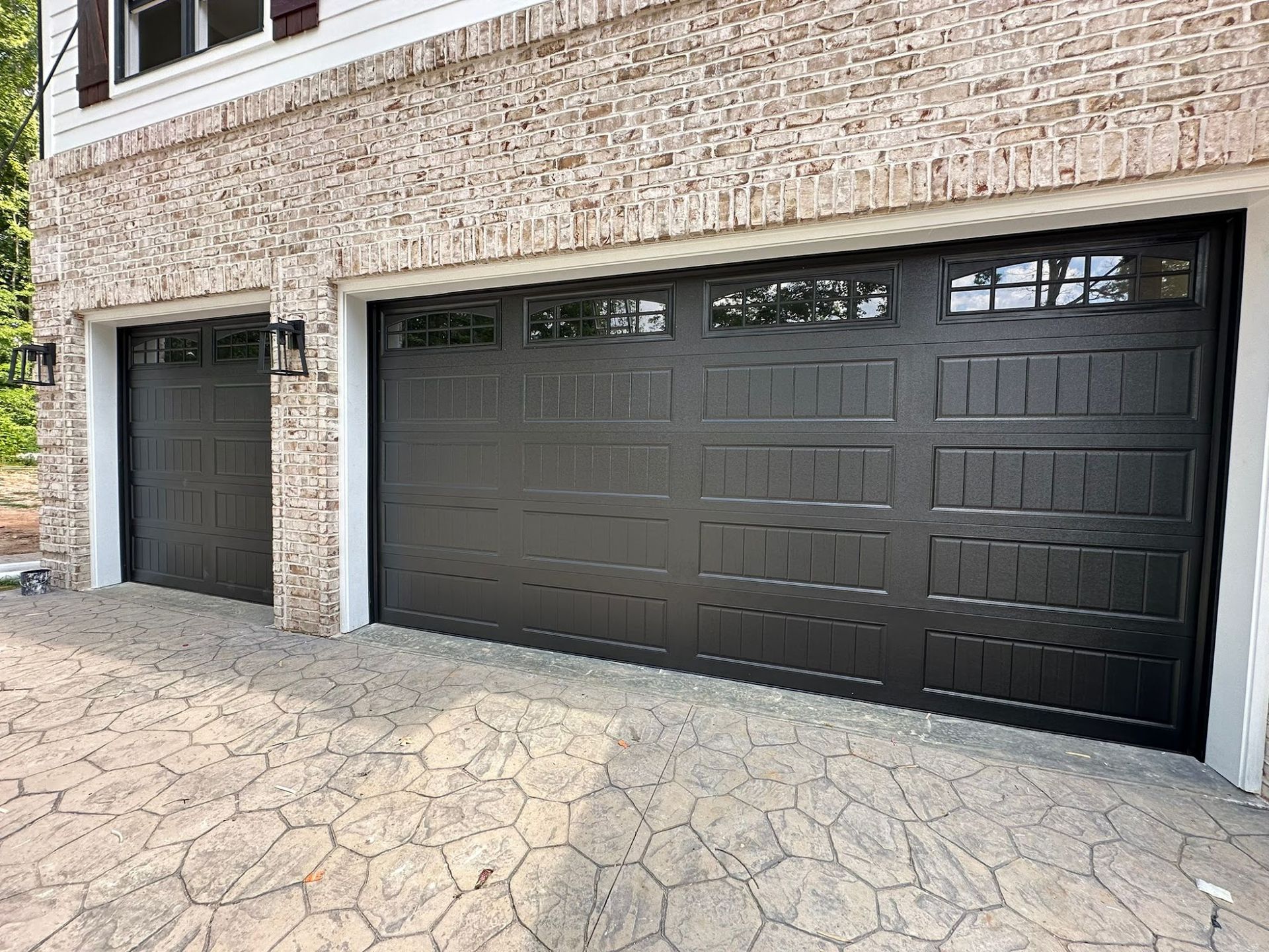 Two black garage doors with brick and stamped concrete driveway.