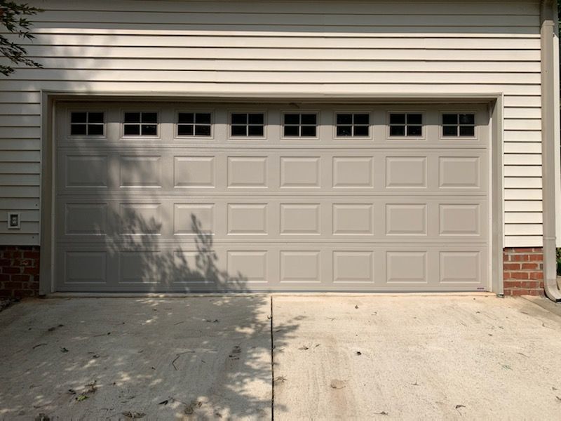 Tan garage door with windows, on a concrete driveway. Beige siding above.