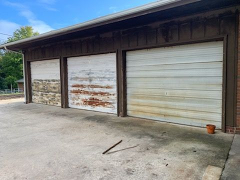 Three weathered garage doors in a brown building, stained concrete.  A fallen stick in foreground.