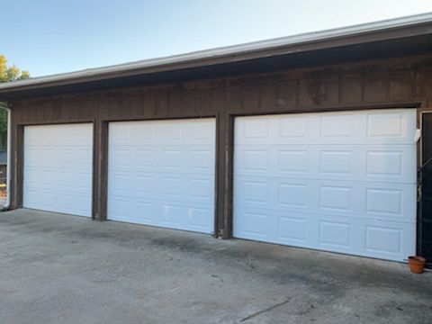 Three white garage doors on a brown building.