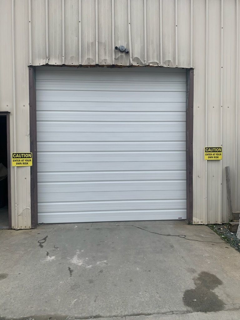 White garage door in a metal building, concrete approach. Two caution signs.