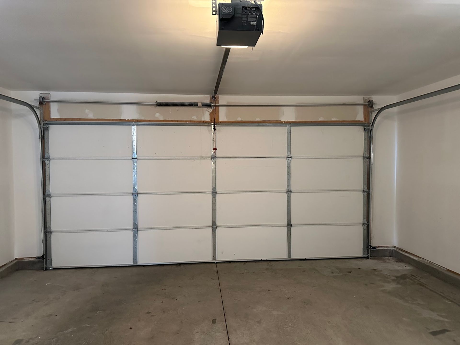 Garage interior with white garage door and opener. Concrete floor, white walls.