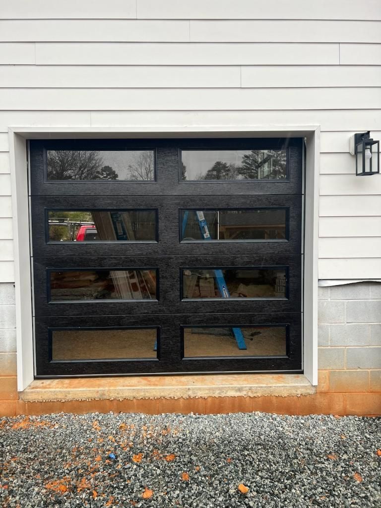 Black glass panel garage door in a white-walled building with a gravel foreground.