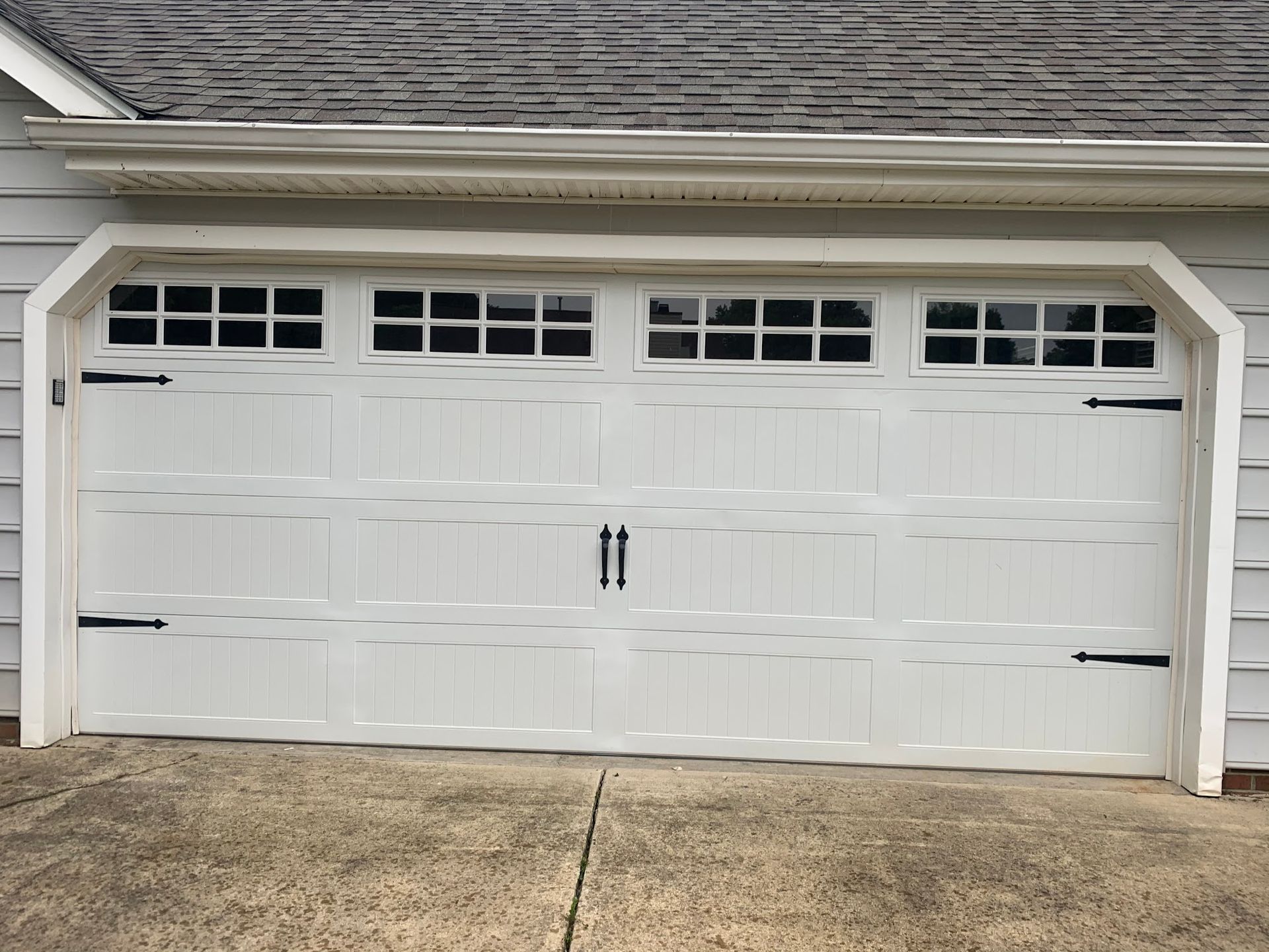 White garage door with windows, decorative black hardware, and gray concrete driveway.