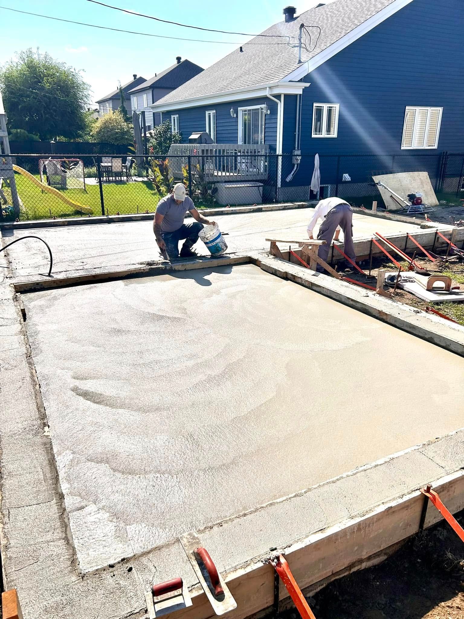 Un homme est assis sur une dalle de béton devant une maison.