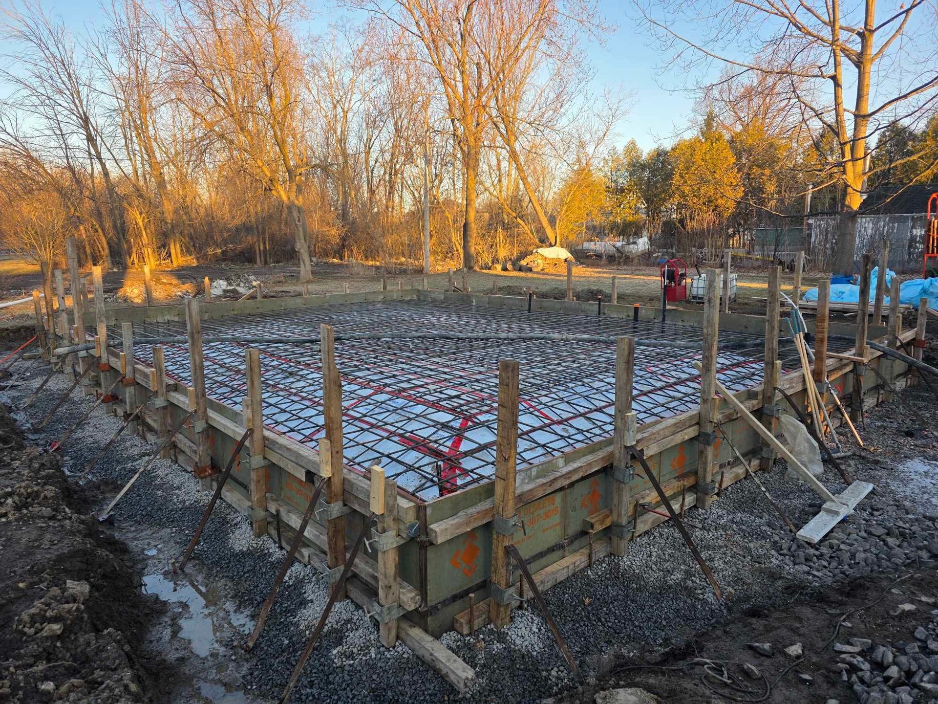 Une fondation en béton est en cours de construction dans un champ avec des arbres en arrière-plan.