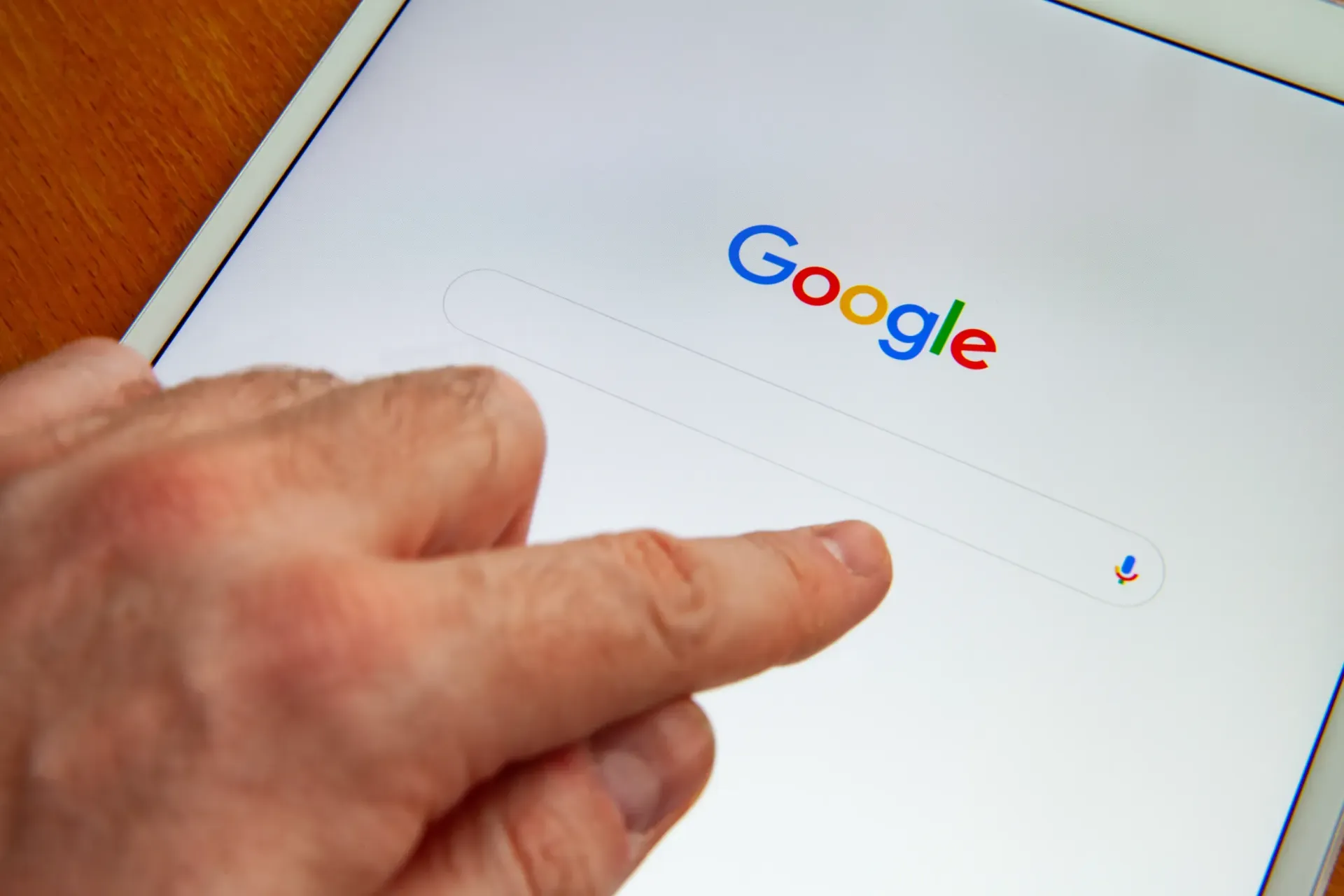 A person is pointing at the google search bar on a tablet.