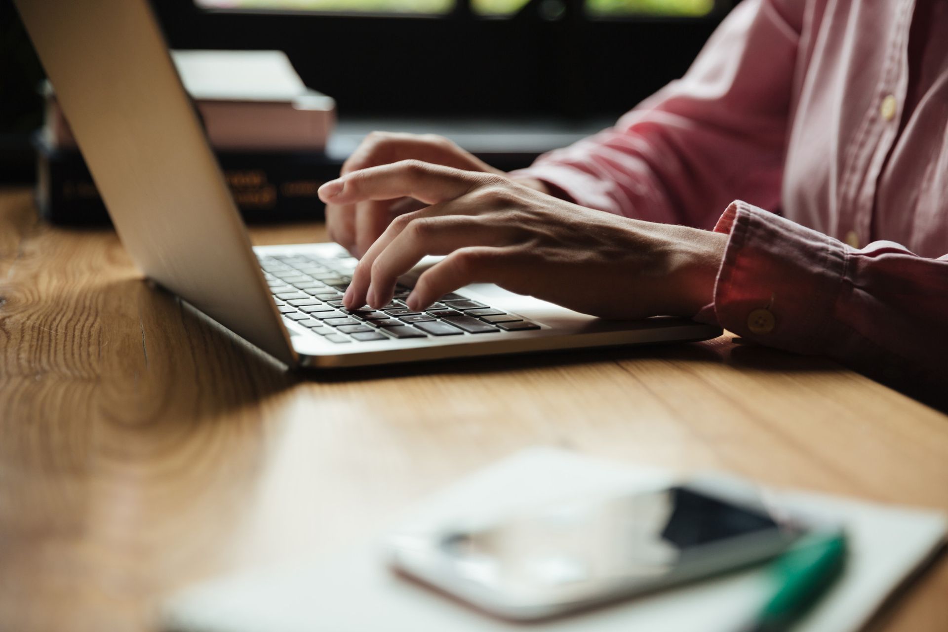 A person is typing on a laptop computer on a wooden table.