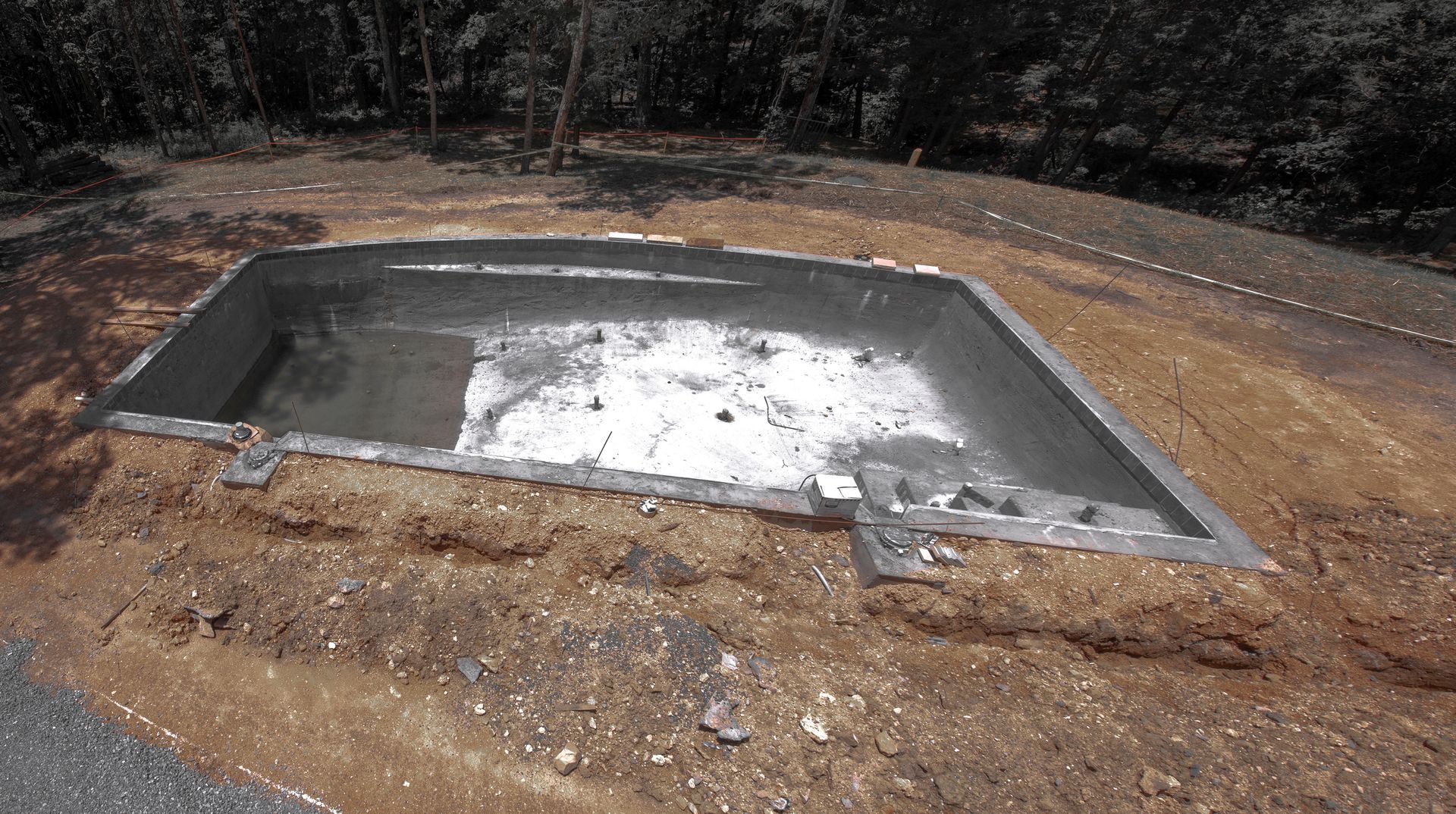 A large concrete pool is sitting in the middle of a dirt field.