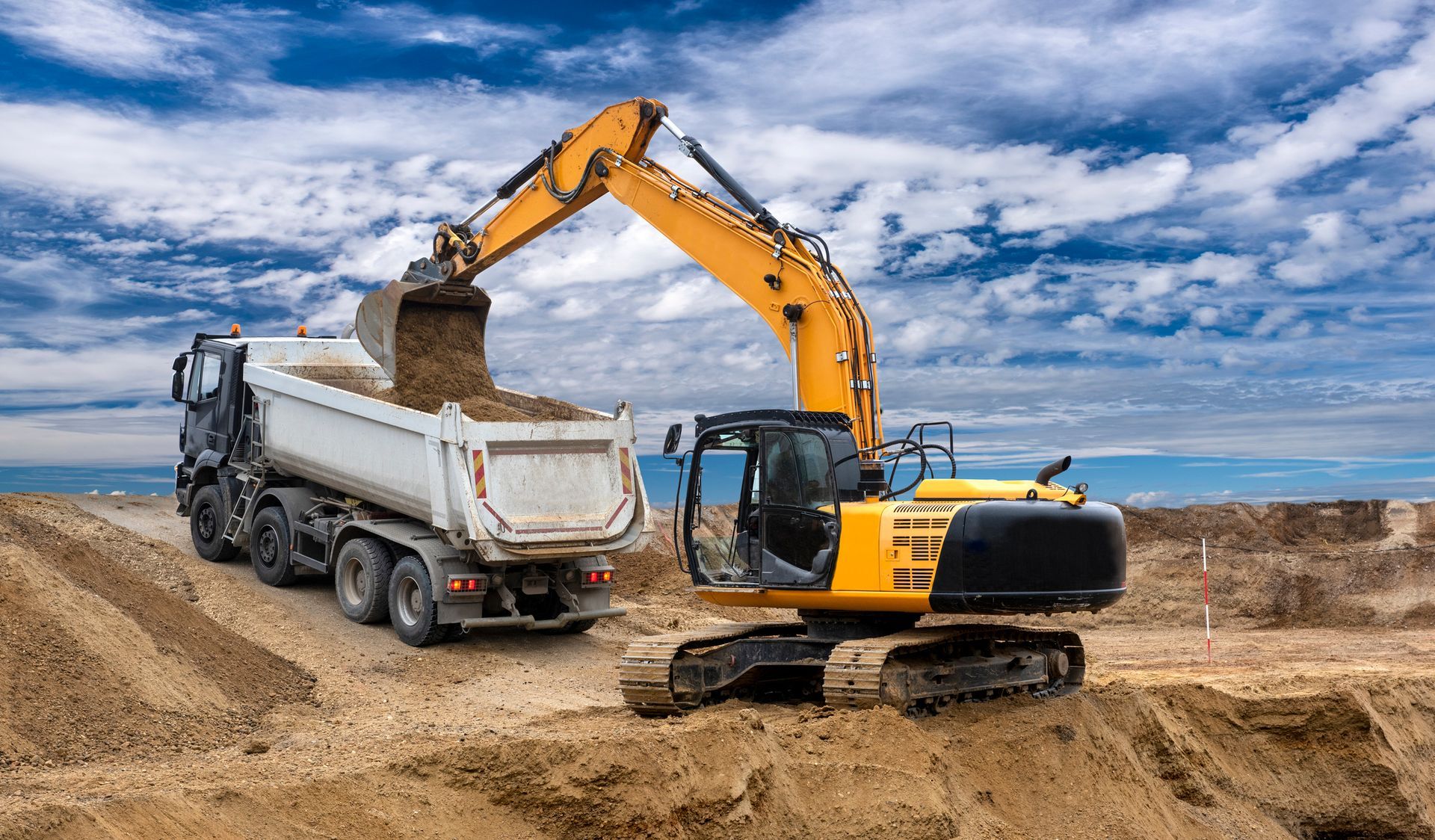 An excavator is loading sand into a dump truck at a construction site.