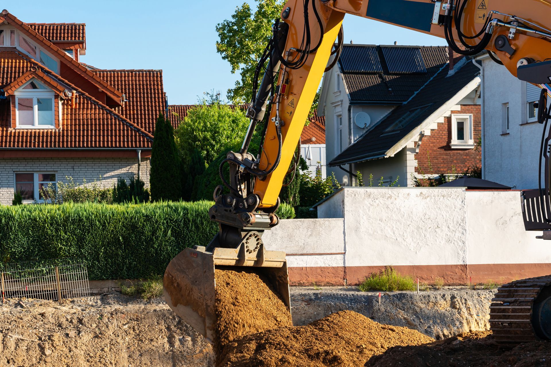 An excavator is digging a hole in the ground in front of a house.