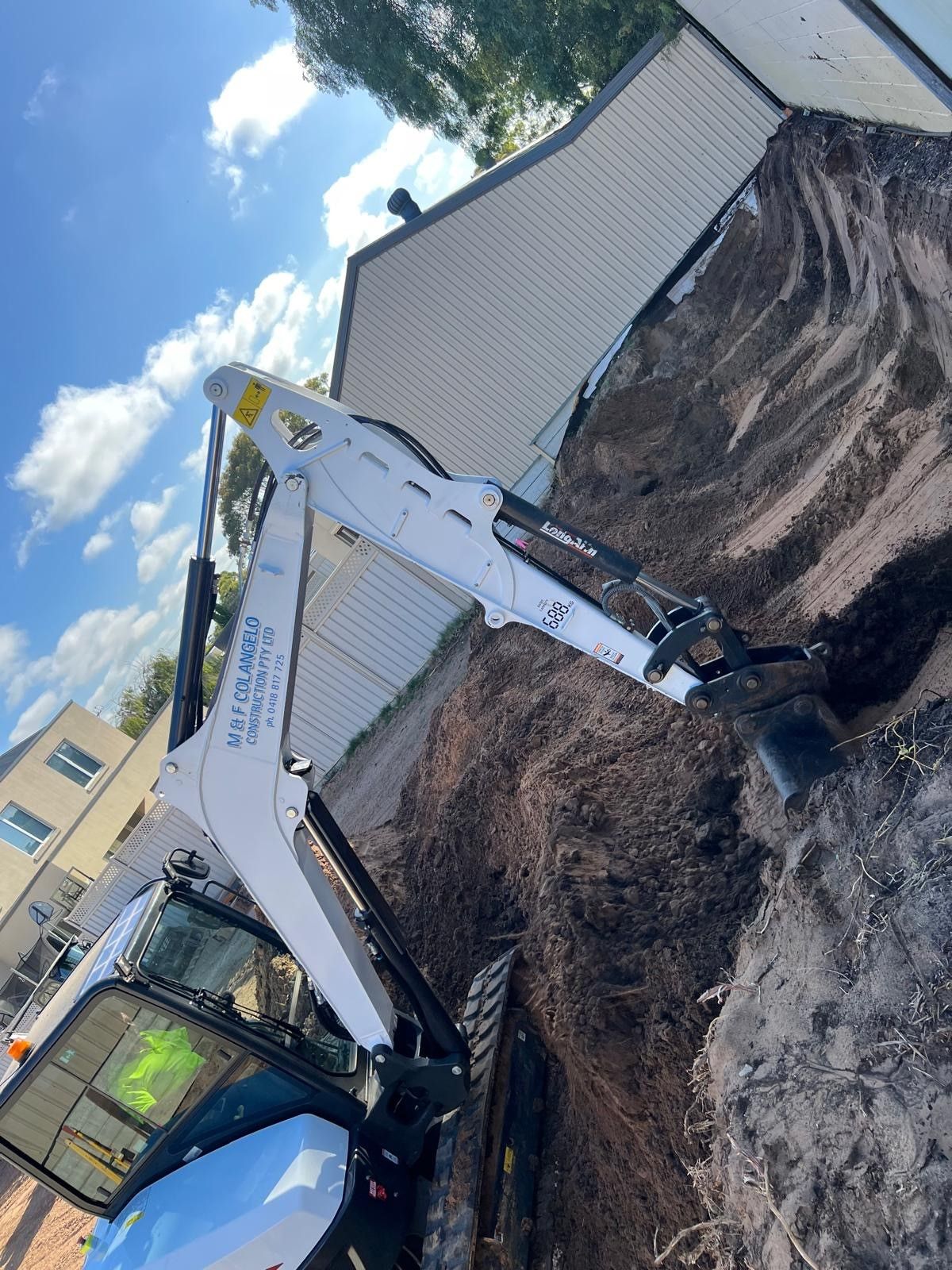 A white excavator is digging a hole in the dirt.