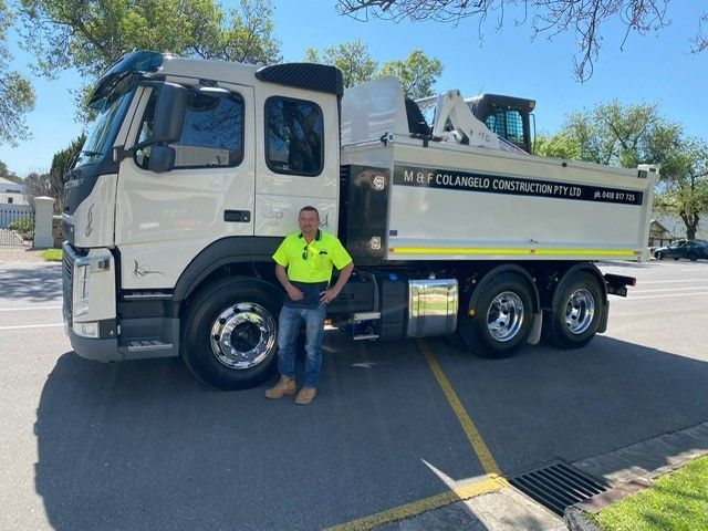 A man is standing next to a dump truck in a parking lot.