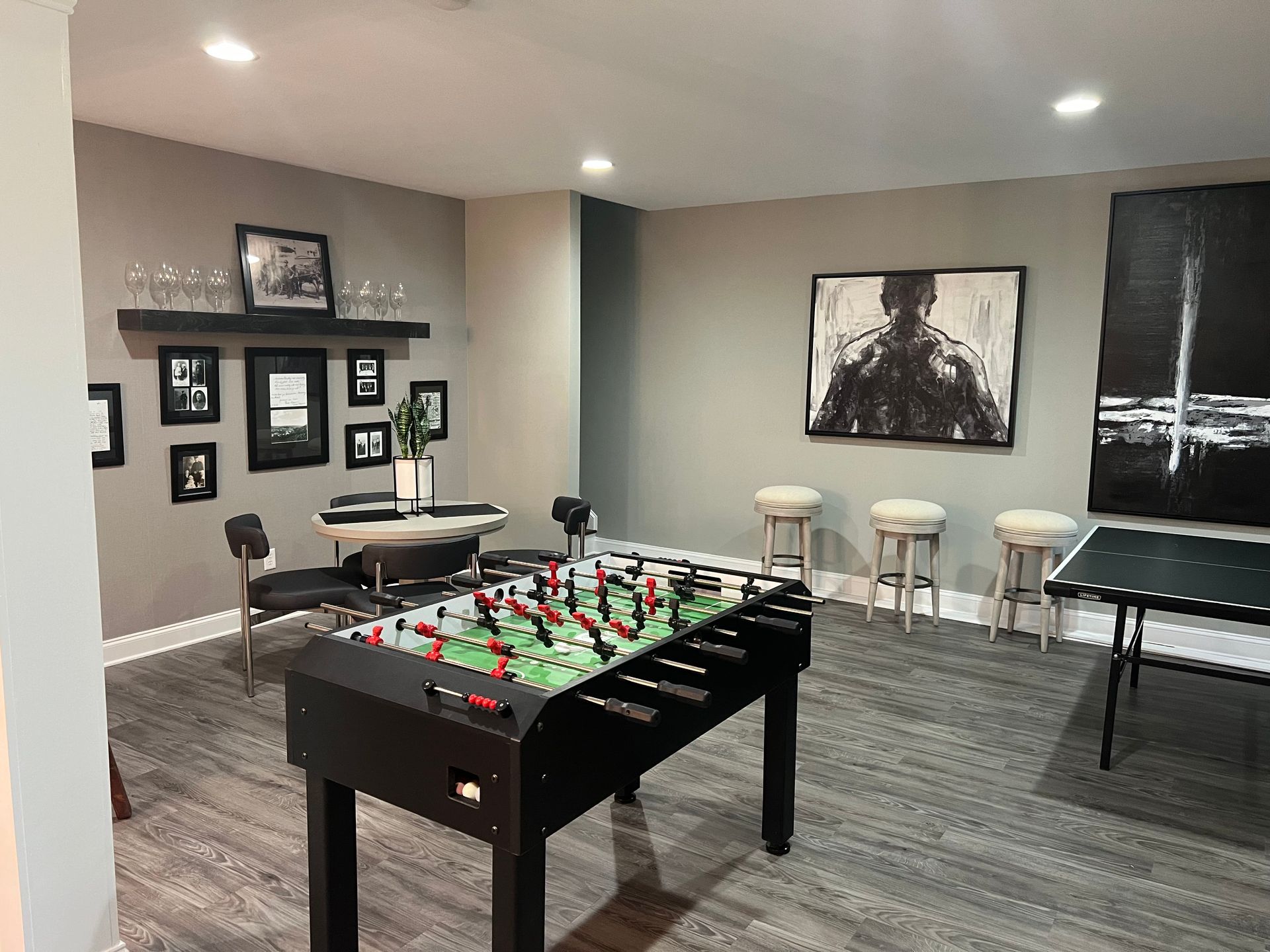 Game room with foosball table, artwork, bar stools, small table, and framed photos on the wall.