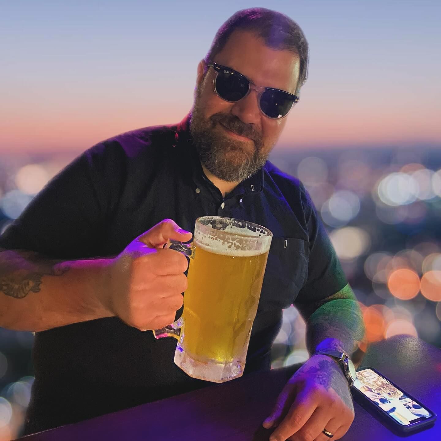 A man wearing sunglasses is holding a mug of beer