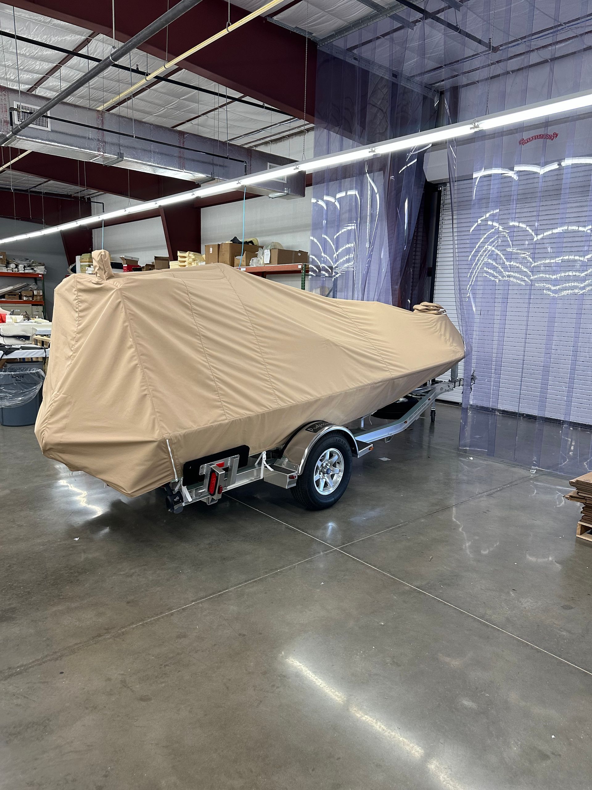 A boat with a cover on it is sitting on a trailer in a warehouse.