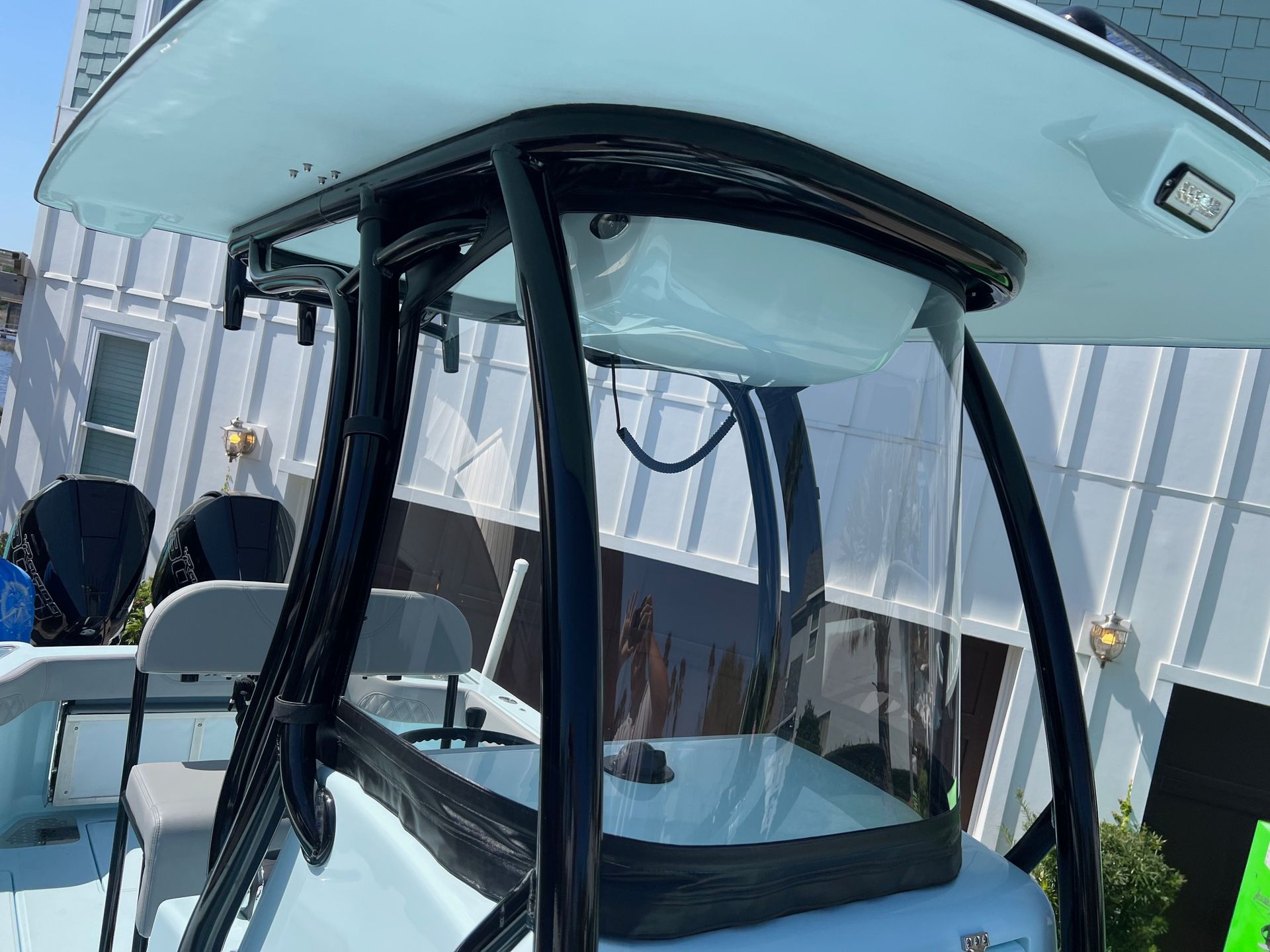 A white boat with a black roof is parked in front of a white house.