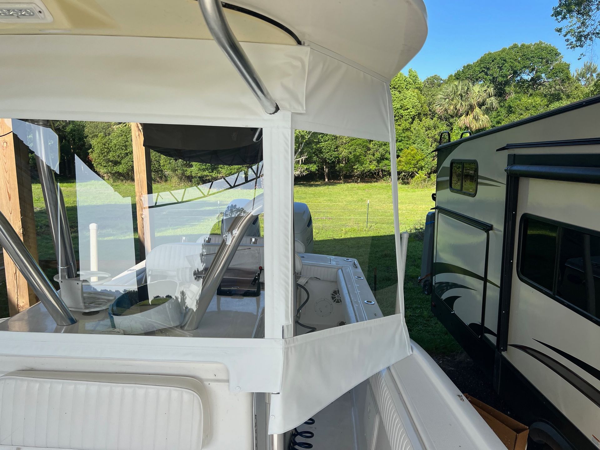 A white boat is parked next to a trailer in a field.
