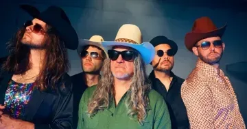 Five men wearing hats and sunglasses pose against a blue background.
