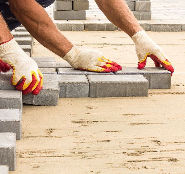 a man wearing gloves is laying bricks on a sidewalk .