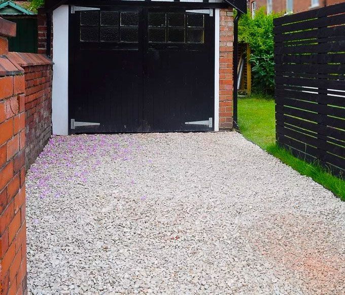 a gravel driveway leads to a black garage door