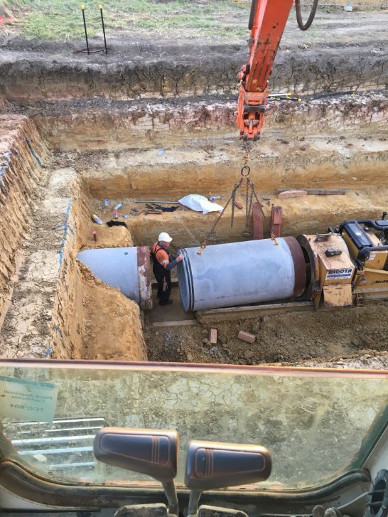 A large pipe is being lifted by a crane in a trench.