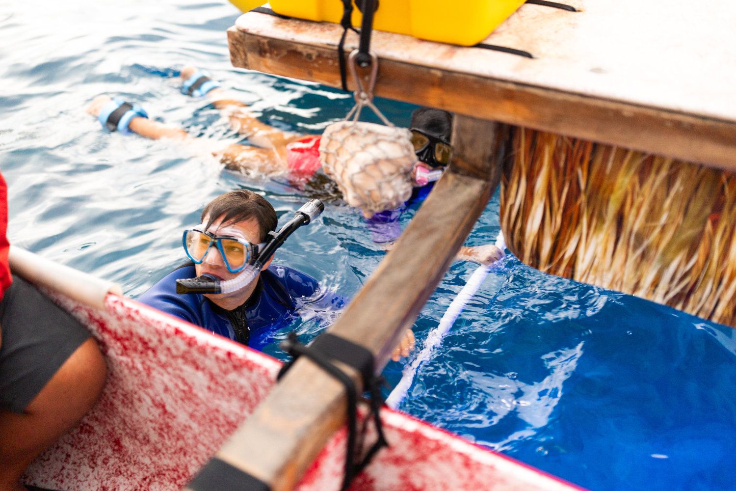 Person snorkeling in blue water near a boat; another person visible further back.