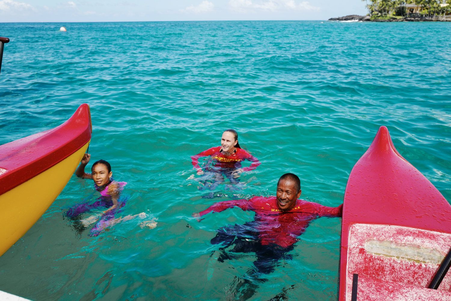 People swimming in turquoise water near colorful boats.