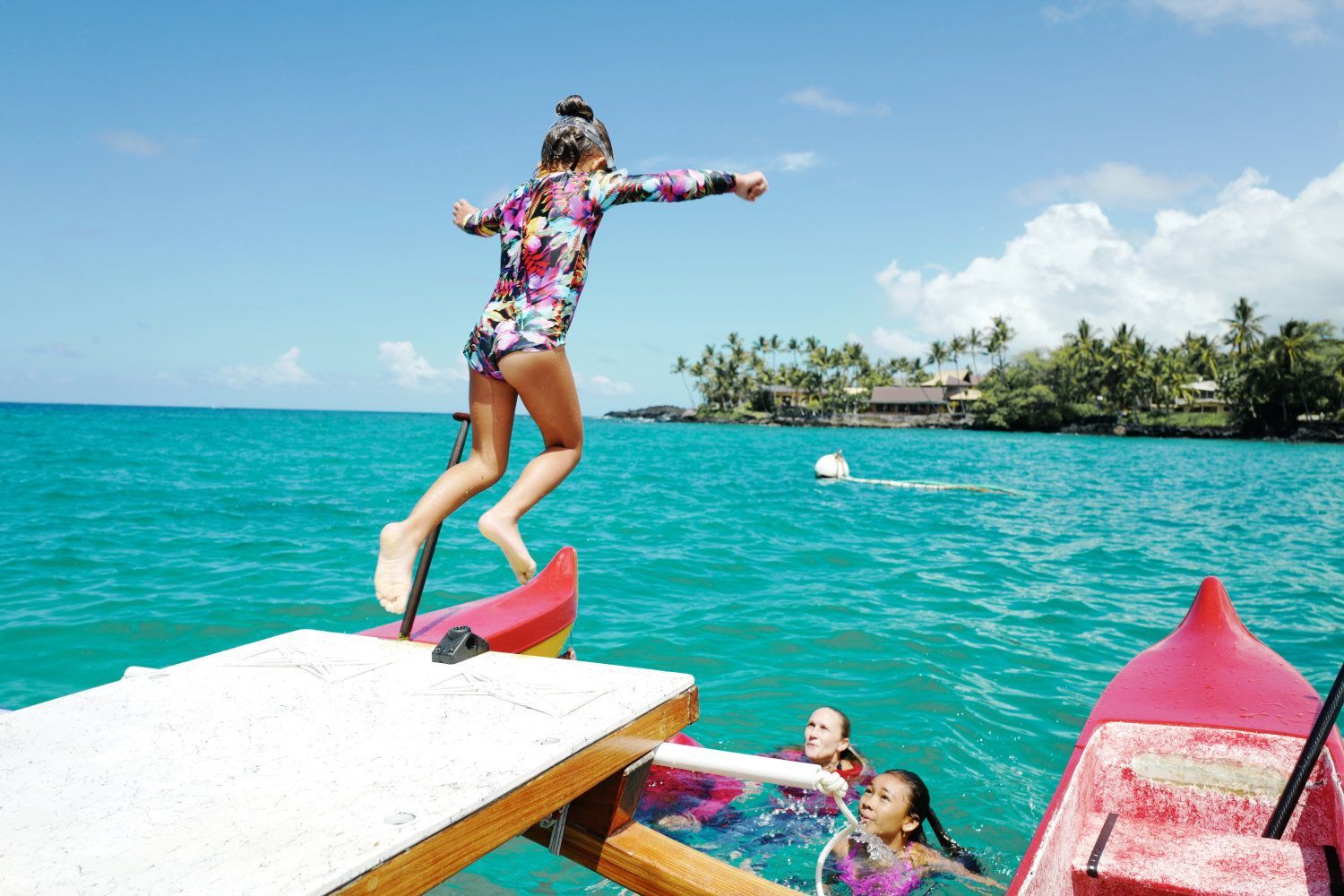 Girl in floral rash guard jumps into turquoise water from a white dock.