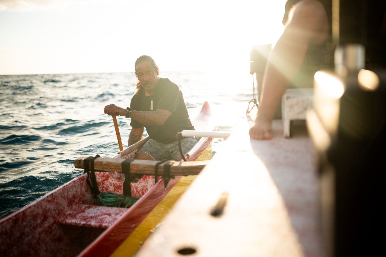 Man rowing a canoe on the ocean, sun shining, white boat with colorful trim.